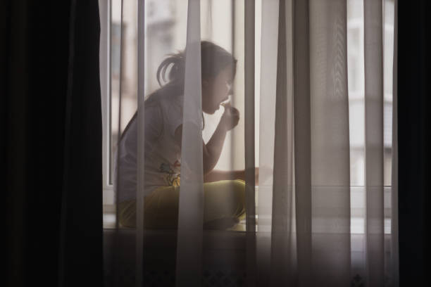 small girl in white t-shirt and yellow leggings sits on window sill, indulging in quiet snack - junk food stock pictures, royalty-free photos & images
