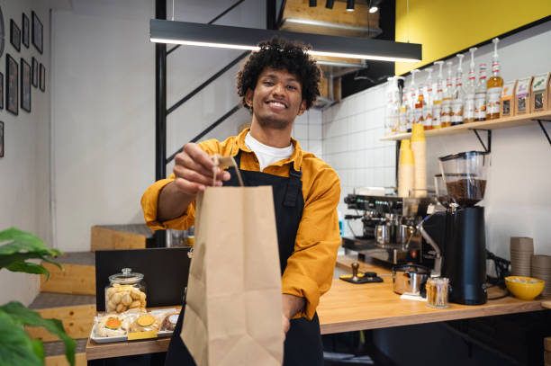 smiling barista holding takeaway bag at coffee shop - junk food stock pictures, royalty-free photos & images
