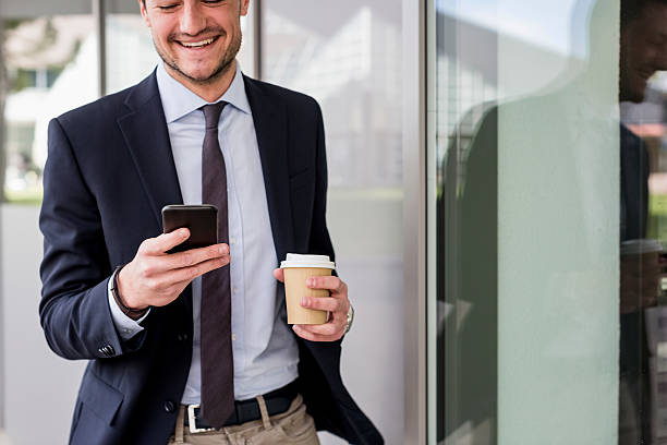 smiling businessman looking at cell phone outdoors - junk food stock pictures, royalty-free photos & images