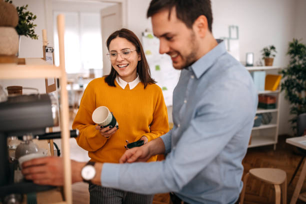 smiling colleagues making coffee in cafeteria at office - coffee stockfoto's en -beelden