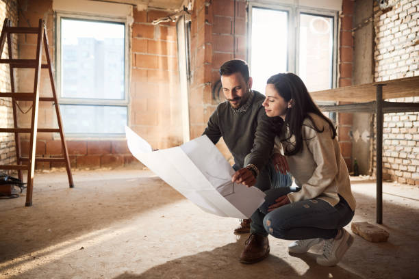 smiling couple analyzing plans at their renovating apartment. - home decoration stock pictures, royalty-free photos & images