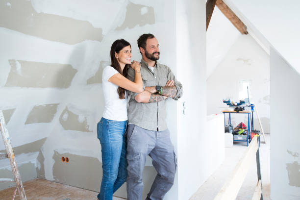 smiling couple in attic to be renovated looking out of window - home decoration stock pictures, royalty-free photos & images