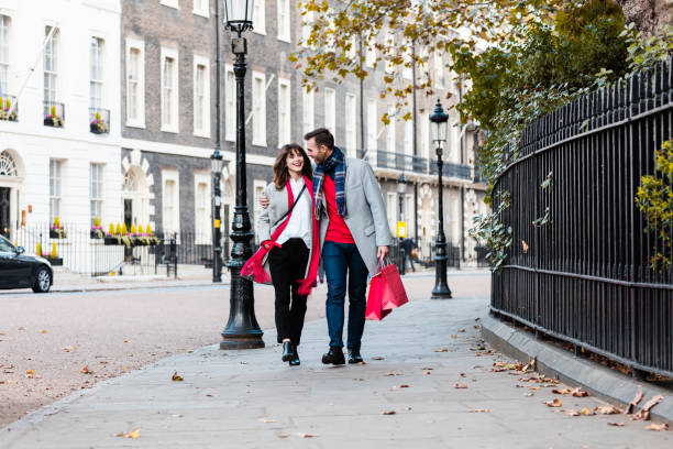 smiling couple walking along the street with shopping bags - fashion stock pictures, royalty-free photos & images