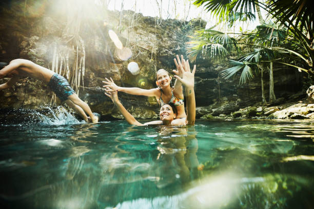 smiling daughter sitting on mothers shoulders while swimming together with family in cenote - travel stock pictures, royalty-free photos & images