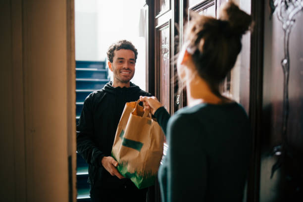 smiling delivery man delivering bag to woman standing at doorway - food stock pictures, royalty-free photos & images