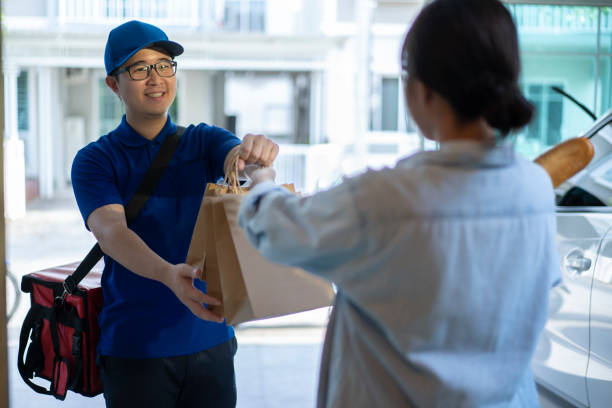 smiling delivery man delivers food to a woman standing at the door. - food stock pictures, royalty-free photos & images