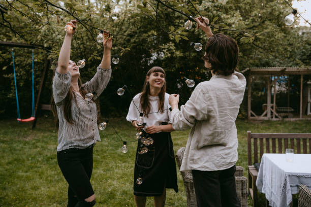 smiling friends hanging lighting equipment in yard during dinner party - garden decoration stock pictures, royalty-free photos & images