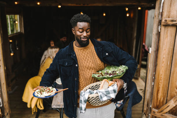 smiling man balancing food while standing at doorway during social gathering - food photos et images de collection