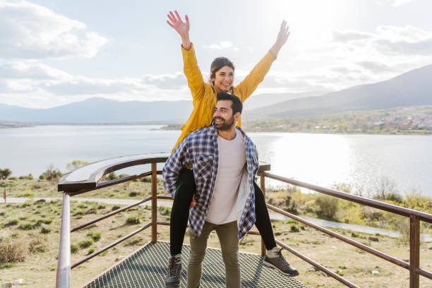 smiling man giving piggyback ride to girlfriend at observation point - travel photos et images de collection