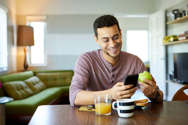 smiling man using mobile phone while holding apple - food stock pictures, royalty-free photos & images