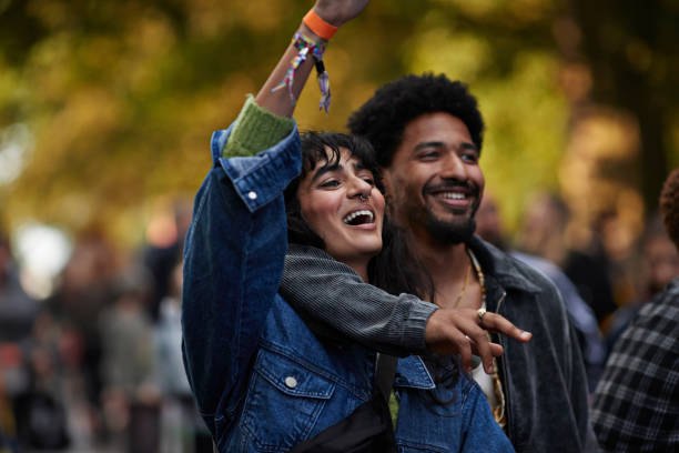 smiling man with arm around girlfriend raising hand - concert stock-fotos und bilder