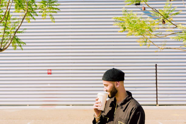 smiling man with coffee to go in front of industrial building - junk food stock pictures, royalty-free photos & images