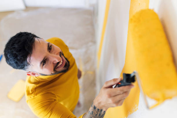 smiling man with paint roller painting wall in living room - home decoration stock pictures, royalty-free photos & images