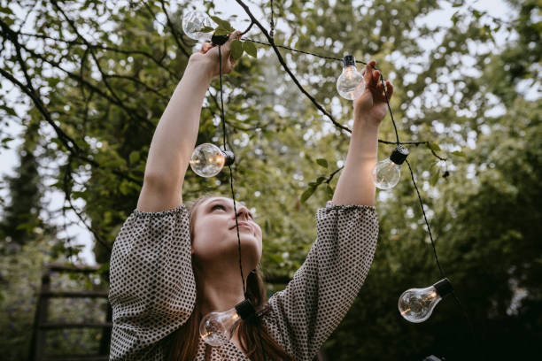 smiling woman hanging lighting equipment in yard during dinner party - garden decoration stock pictures, royalty-free photos & images