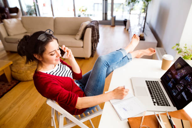 smiling woman on the phone working at desk at home - junk food stock pictures, royalty-free photos & images