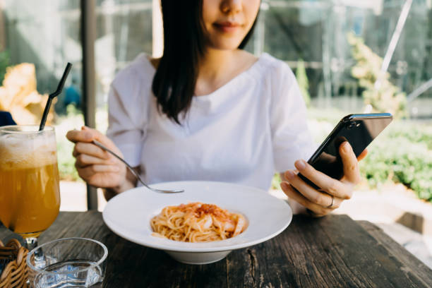 smiling woman using her mobile phone while having meal at a cafe outdoors - junk food stockfoto's en -beelden