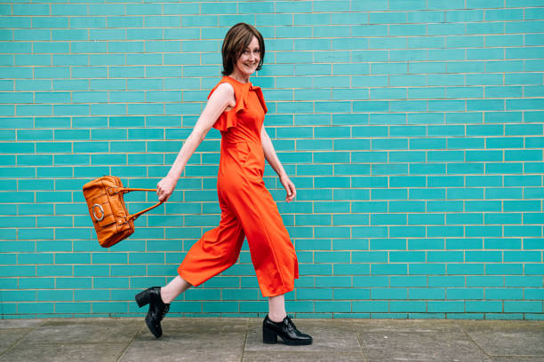 smiling woman wearing jumpsuit walking by brick wall - fashion stock pictures, royalty-free photos & images