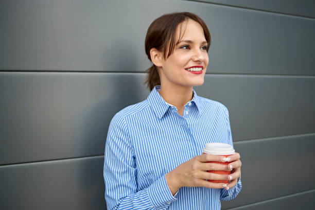 smiling young white caucasian woman on the move drinking coffee from disposable cup. - junk food stock pictures, royalty-free photos & images