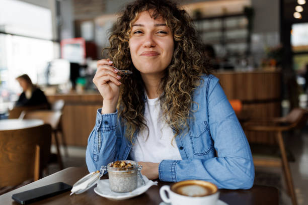 smiling young woman eating chia pudding for breakfast at cafe - food stock pictures, royalty-free photos & images