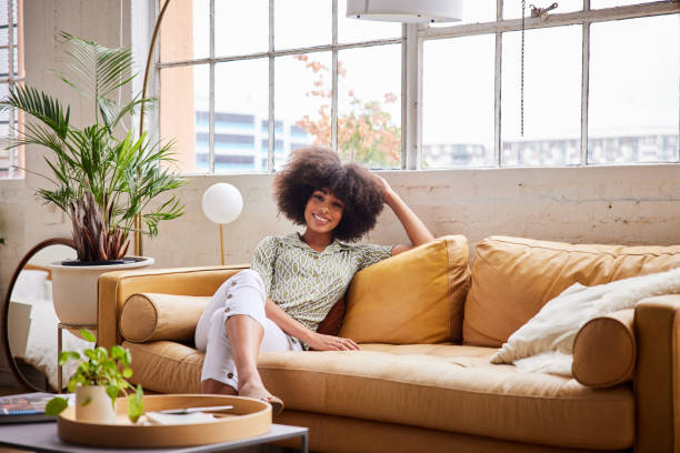 smiling young woman relaxing on a comfortable sofa at home in the afternoon - home decoration stock pictures, royalty-free photos & images