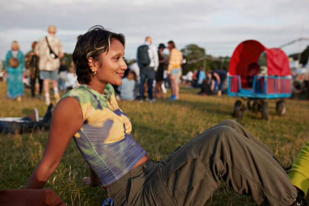smiling young woman sitting on grass at festival - concert stock pictures, royalty-free photos & images