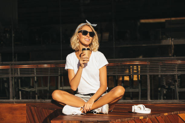 smiling young woman with cell phone and takeaway drink at the cafe - junk food stock pictures, royalty-free photos & images