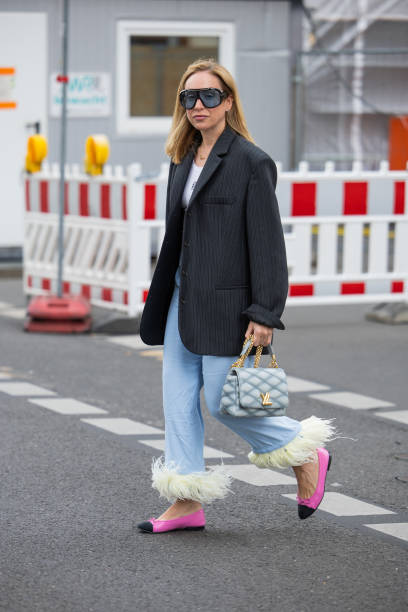 Sonia Lyson wears black oversized striped blazer, blue Louis Vuitton bag, wide leg denim jeans with fringes, pink shoes, Tom Ford sunglasses during...