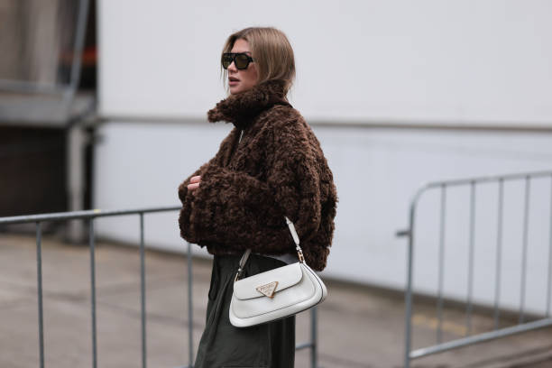 Sophia Geiss is seen wearing squared black aviator sunglasses with olive lenses from Vehla Eyewear, a silver nose ring, a cropped brown faux...