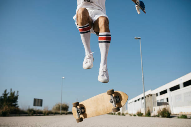 sportive man jumping above ground with skateboard performing trick - fashion stock-fotos und bilder
