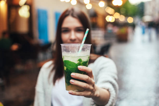 street portrait of young woman holding a glass of mojito in hands. blurred restaurant in background. summer lifestyle, drinks concept. - junk food stock pictures, royalty-free photos & images
