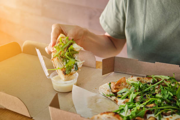 stylish girl adds sauce to a slice of vegetarian pizza. italian cuisine. sliced pizza in paper packaging on a wooden table. delicious lunch, snack, fast food. - junk food stock pictures, royalty-free photos & images