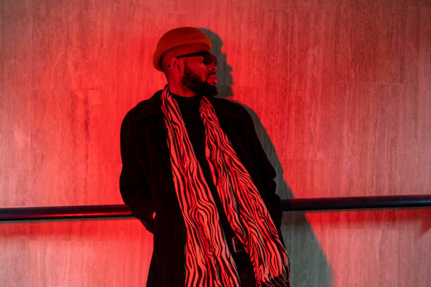 stylish hipster black man in sunglasses stands leaning against wall in underpass lit by red light - fashion stock pictures, royalty-free photos & images