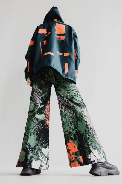 stylish woman wearing a multi-colored jacket and flare pants with black boots, is seen from the back abstract portrait - fashion stock pictures, royalty-free photos & images