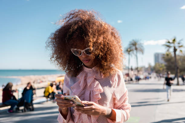 stylish young woman using cell phone at seaside promenade - fashion stock-fotos und bilder