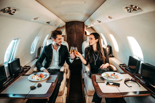 successful couple making a toast with champagne glasses while having canapes aboard a private airplane - travel stock pictures, royalty-free photos & images