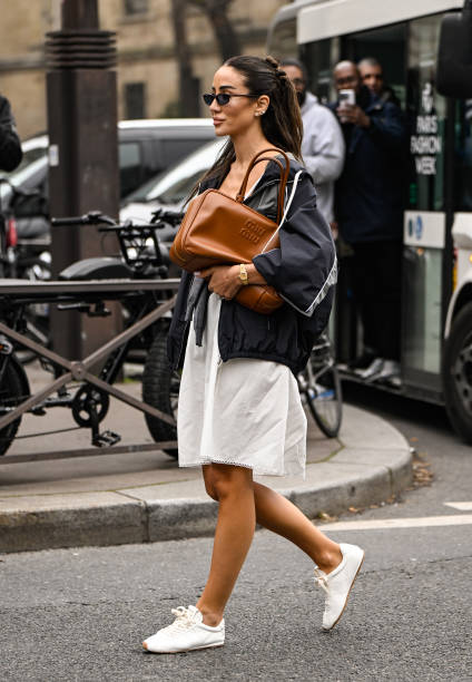 Tamara Kalinic is seen wearing a gray Miu Miu top, black Miu Miu jacket, white skirt, white sneakers and brown Miu Miu bag and black sunglasses...