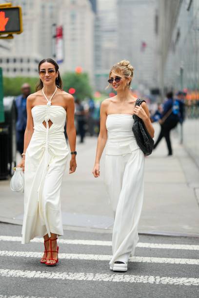 Tamara Kalinic wears a white gathered dress ; Xenia Adonts wears a white off-shoulder top, white palazzo flared pants, outside Proenza Schouler,...