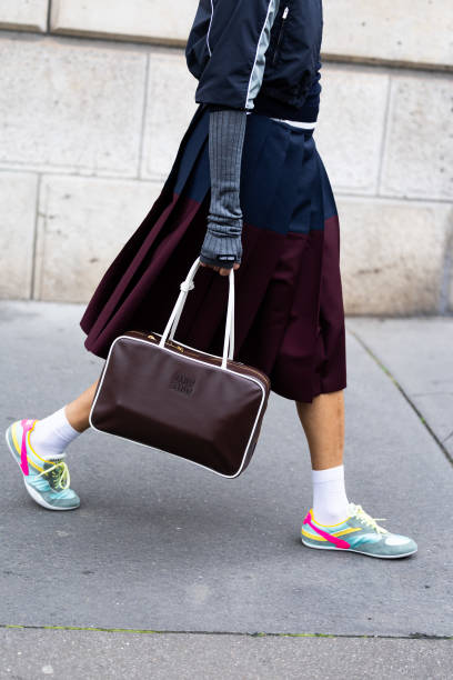 Tamu Mcpherson wears a blue sweater, a grey and dark grey jacket, grey long gloves, a blue and bordeaux pleated maxi skirt, a brown leather Miu Miu...