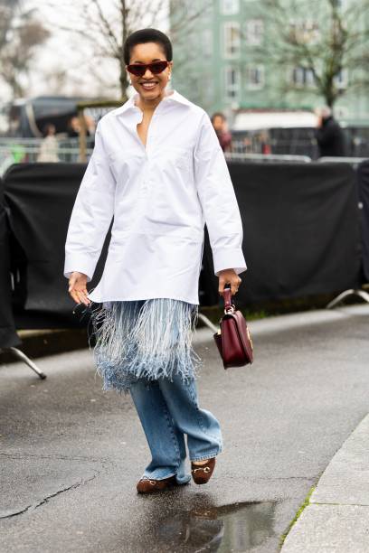 Tamu McPherson wears bordeaux sunglasses, silver hoop earrings, a white oversized shirt with fringes, a bordeaux Gucci leather bag, blue jeans and...