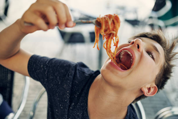 teenage boy enjoying eating spaghetti very much. - food stock pictures, royalty-free photos & images