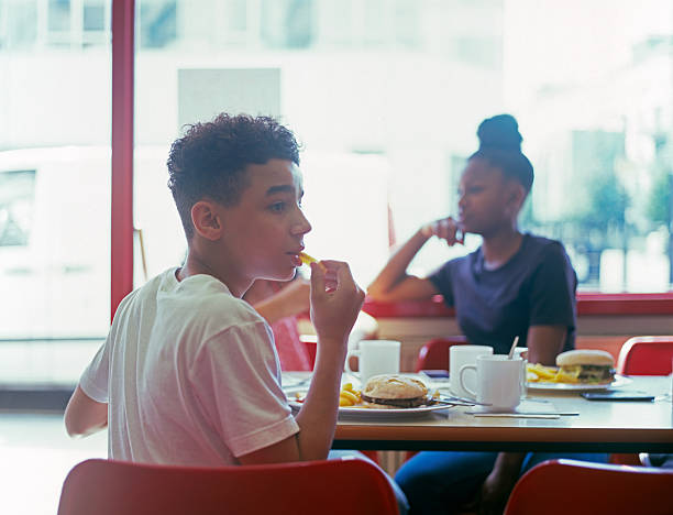teenage boy in cafe eating burger and chips - junk food stockfoto's en -beelden