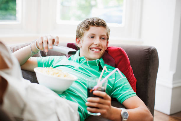 teenage boy with snacks holding remote control - junk food stockfoto's en -beelden