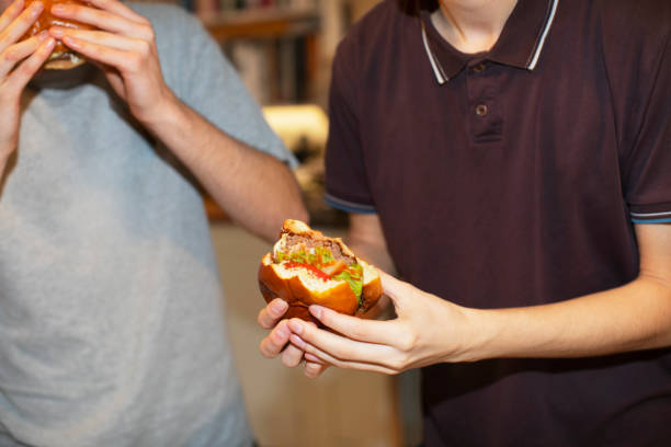 teenage boys eating hamburgers - junk food stock pictures, royalty-free photos & images