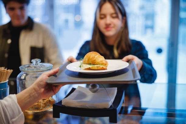 teenage girl in plaid shirt taking croissant sandwich on the counter in cafeteria - junk food stock pictures, royalty-free photos & images