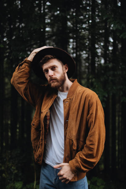 the portrait of a stylish handsome man in a hat in the forest tree background - fashion stock pictures, royalty-free photos & images