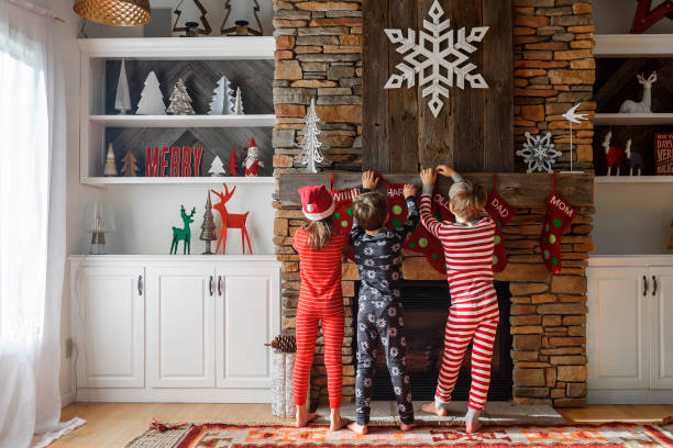 three children hanging up christmas stockings on a fireplace - home decoration stockfoto's en -beelden