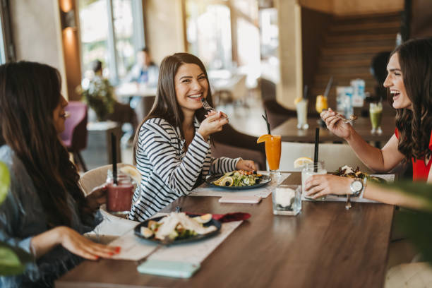 three young cheerful female friends enjoying lunch together at restaurant - food stock pictures, royalty-free photos & images