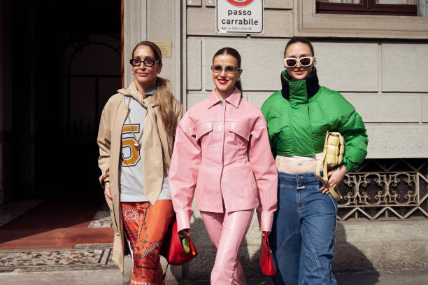 Tiany Kiriloff wears orange skirt, white shirt with the numbers, beige coat and beige scarf and Nina Sandbech wears pink leather matching pants and...