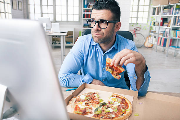 tired businessman eating pizza at the office - junk food stock pictures, royalty-free photos & images