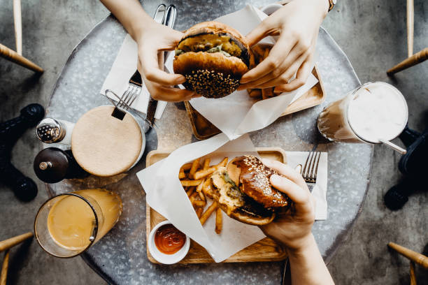 top view of friends having a good time eating burgers with french fries and drinks in a cafe - junk food stock pictures, royalty-free photos & images
